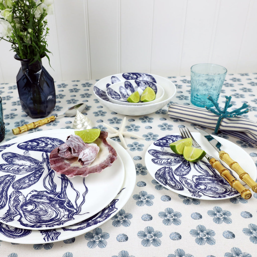 Table setting of Mussel & Oyster plates and bowls.Styled on and around the tableware is bamboo cutlery,napkins and a blue vase