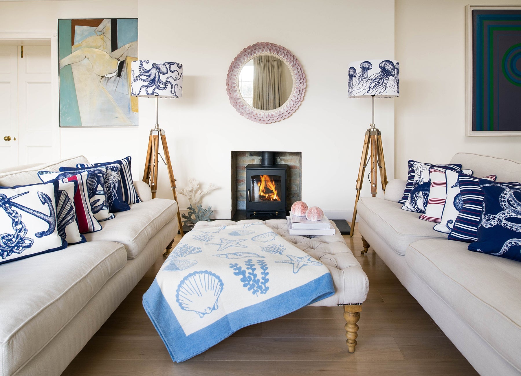 Our Classic Navy Octopus design on a white background on a tripod stand on one side of a fireplace,there is another tripod with a Jellyfish lampshade on the other side.In the photo are two large white sofas with our classic cushions placed on them.There is a wood burner in the fireplace and there is a footstool in the middle of the sofas.