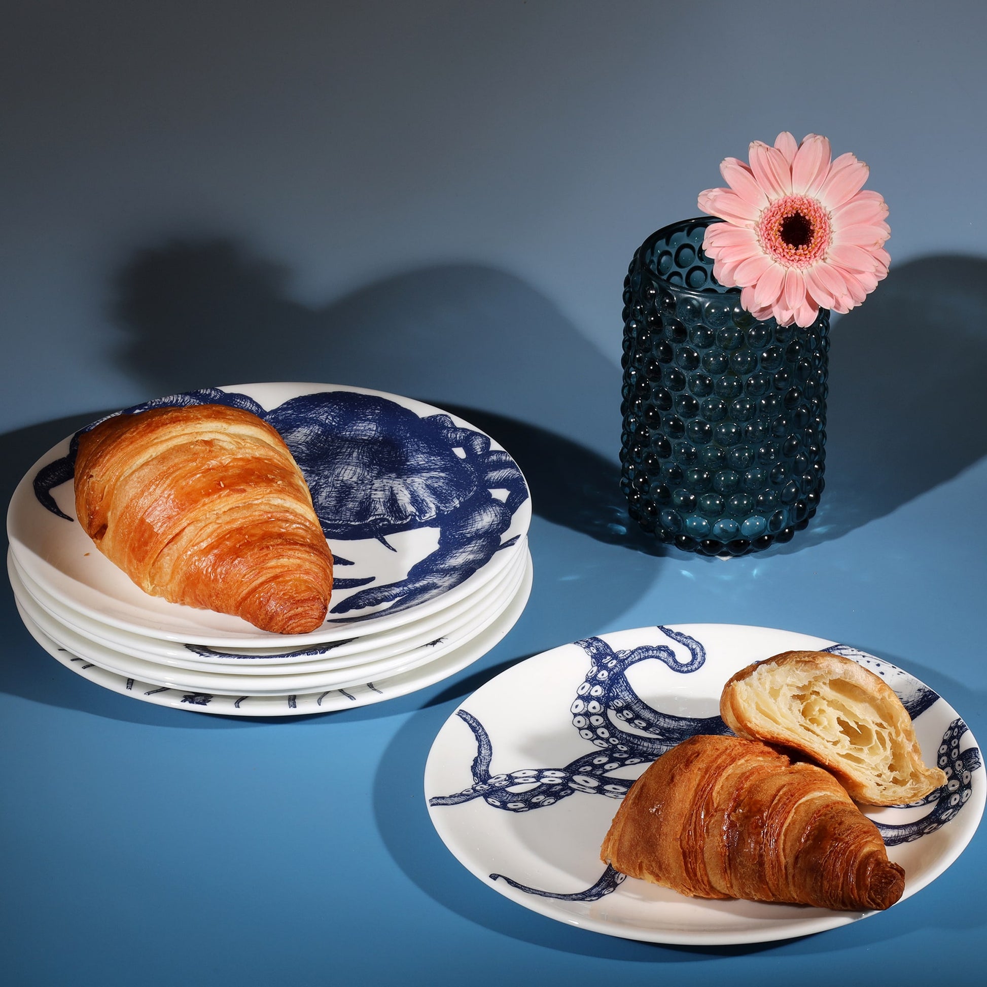 Stacked bone china side plates decorated with croissants next to a petrol blue candle holder