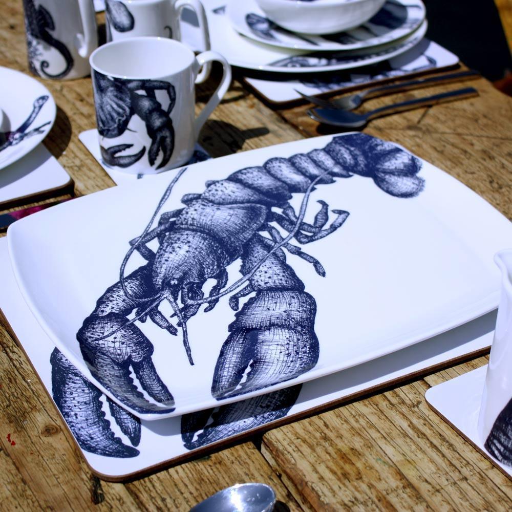 Platter in Bone China in our Classic range in Navy and white in the Lobster design on a outdoor wooden table placed on a tablemat.In the background are other place settings in our classic designs