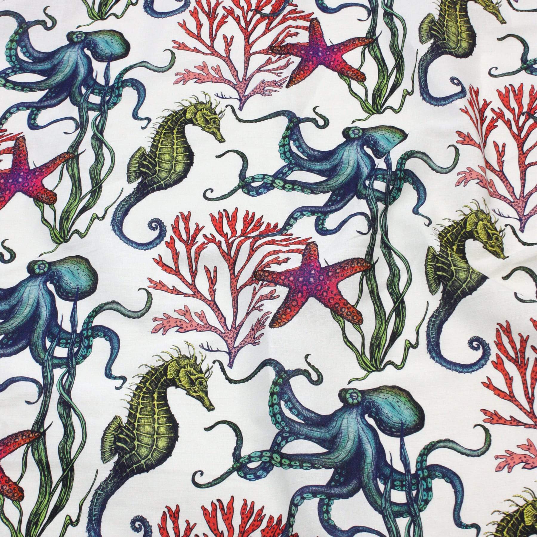 Flat lay of Cream Cornwall’s Rainbow Reef fabric featuring a vibrant underwater design. The pattern includes illustrated octopuses, seahorses, starfish, and red coral, all in vivid shades of blue, green, red, and purple on a white background.