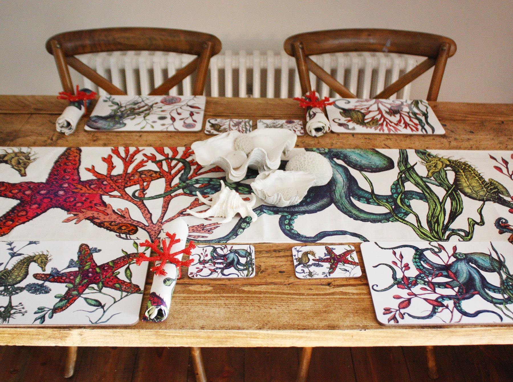 Set of four different coasters in our Reef coloured design with an Octopus,Seahorse,Jellyfish and a Starfish design with matching Placemats.All placed on a table in a place setting,with a matching table runner along the middle of the table.