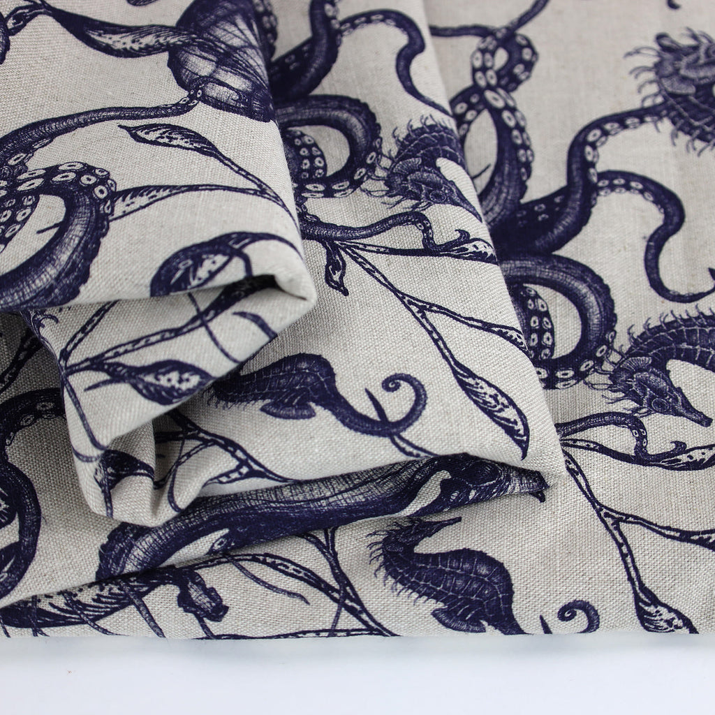 Close-up of folded Cream Cornwall fabric in natural linen, featuring detailed navy illustrations of sea creatures including seahorses and octopuses intertwined with seaweed. The intricate marine design evokes a classic coastal charm with a hand-drawn aesthetic.