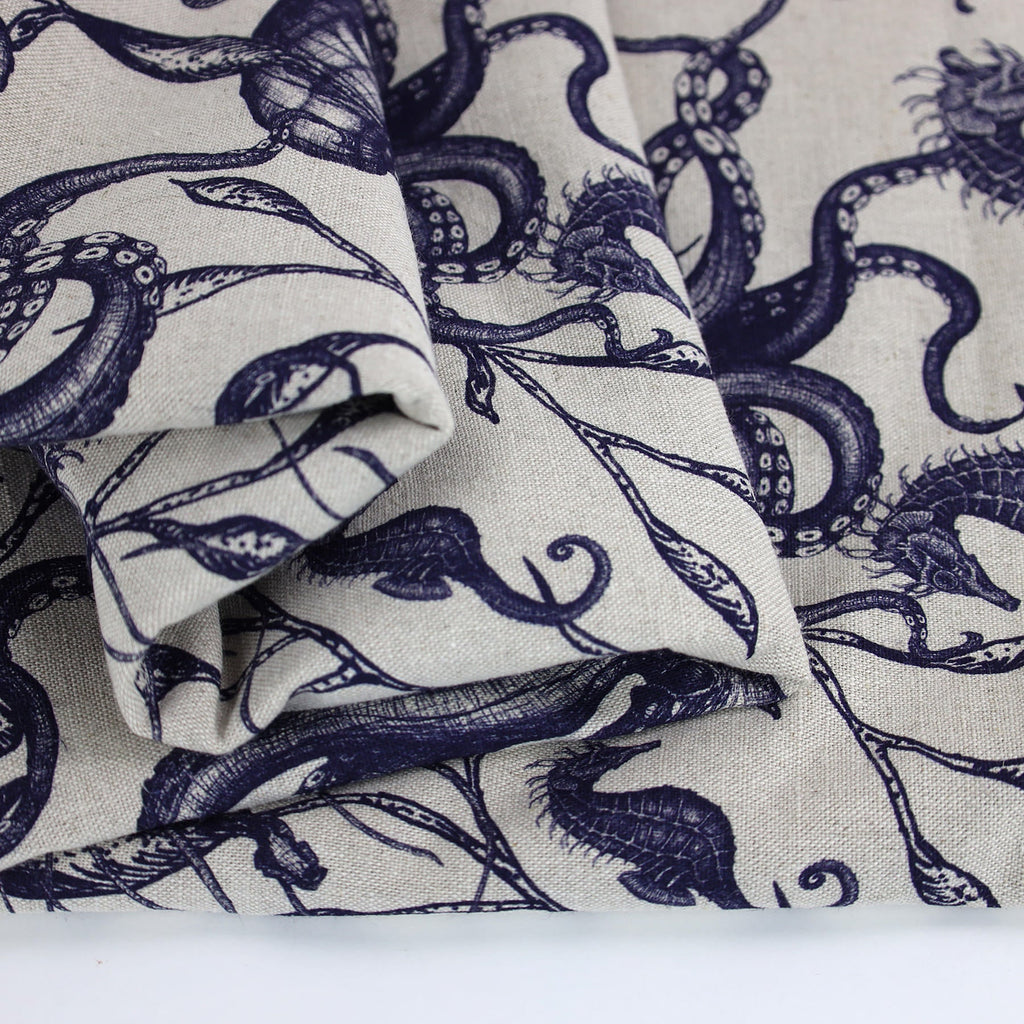 Close-up of folded Cream Cornwall fabric in natural linen, featuring detailed navy illustrations of sea creatures including seahorses and octopuses intertwined with seaweed. The intricate marine design evokes a classic coastal charm with a hand-drawn aesthetic.