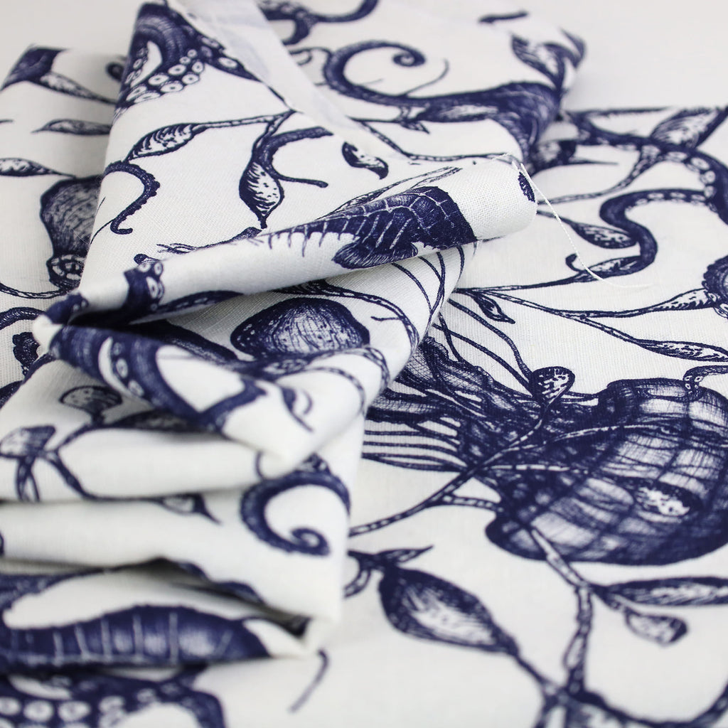 A close-up image of Cream Cornwall’s folded nautical-themed fabric in navy and white. The design features intricately drawn marine elements including seashells, seaweed, and seahorses, printed in a fine illustrative style on soft, natural linen fabric.