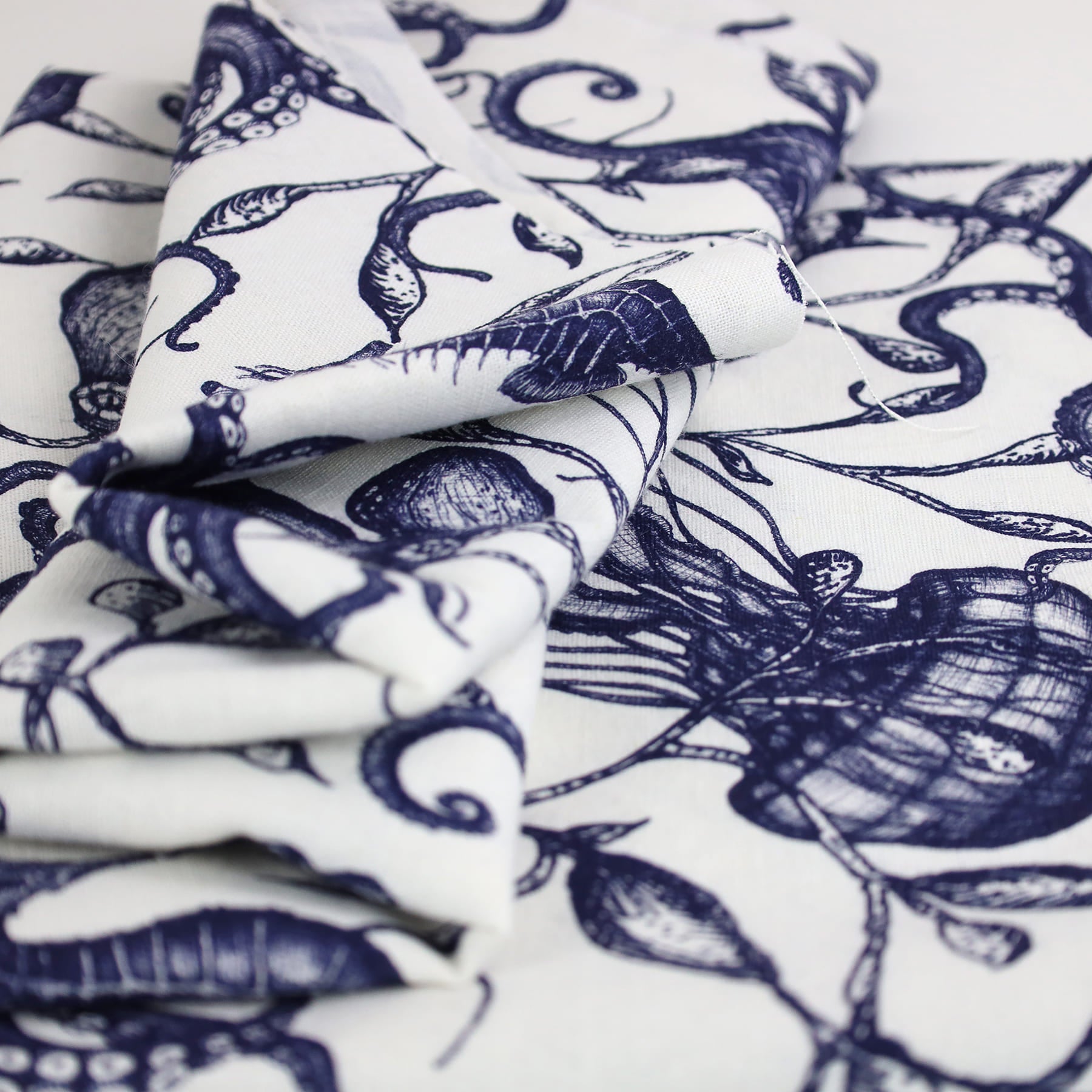 A close-up image of Cream Cornwall’s folded nautical-themed fabric in navy and white. The design features intricately drawn marine elements including seashells, seaweed, and seahorses, printed in a fine illustrative style on soft, natural linen fabric.