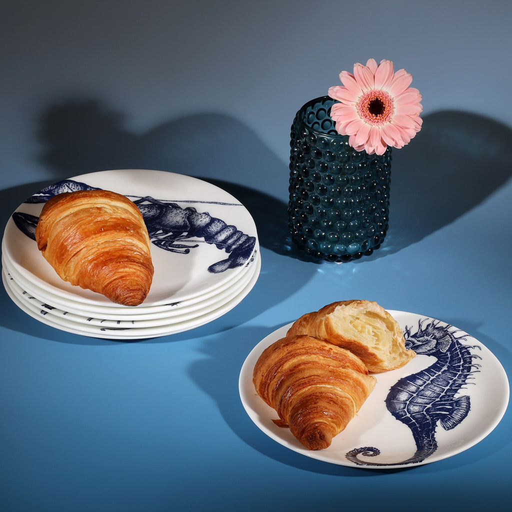 Stacked bone china side plates decorated with croissants next to a petrol blue candle holder