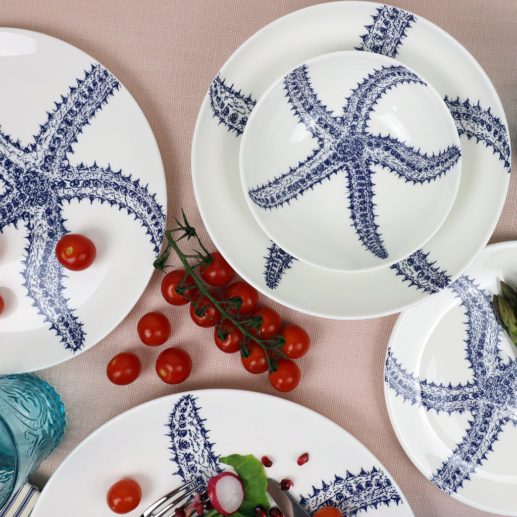 Pasta bowl in Bone China in our Classic range in Navy and white in the Starfish design next to a matching dinner plate and others decorated with brightly coloured food on a blush covered tablecloth