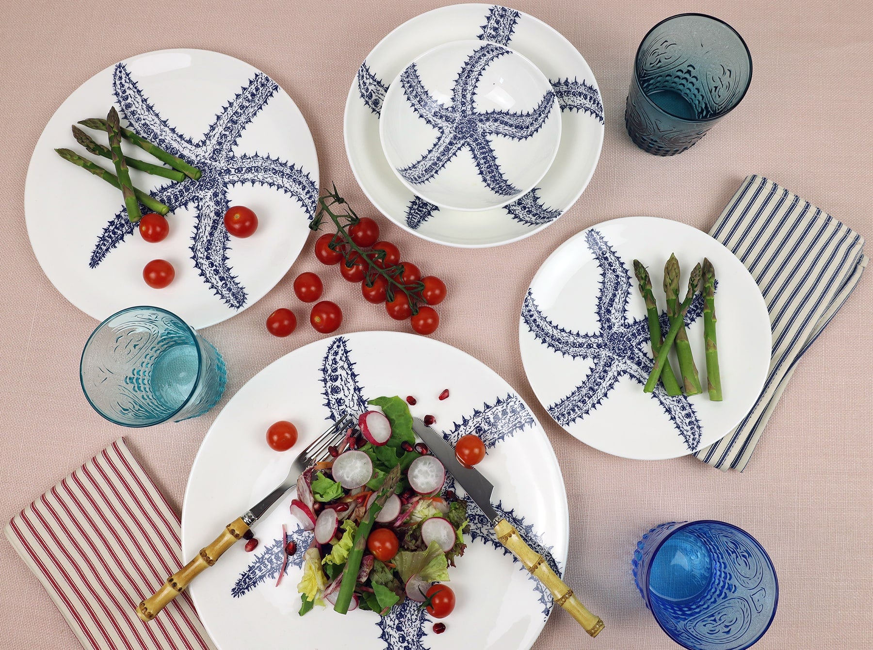Aerial view of Starfish plate on a soft pink tablecloth.On the plate is a radish salad with Bamboo cutlery,to the side are stripe napkins,a glass and other tableware in the Starfish design.