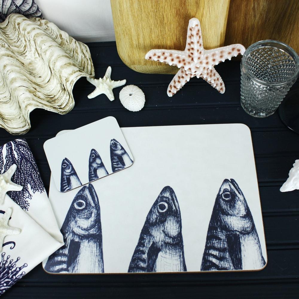 Mackerel Heads Design in Navy on a white Coaster with a matching Placemat.On the table are decorative shells and a matching napkin
