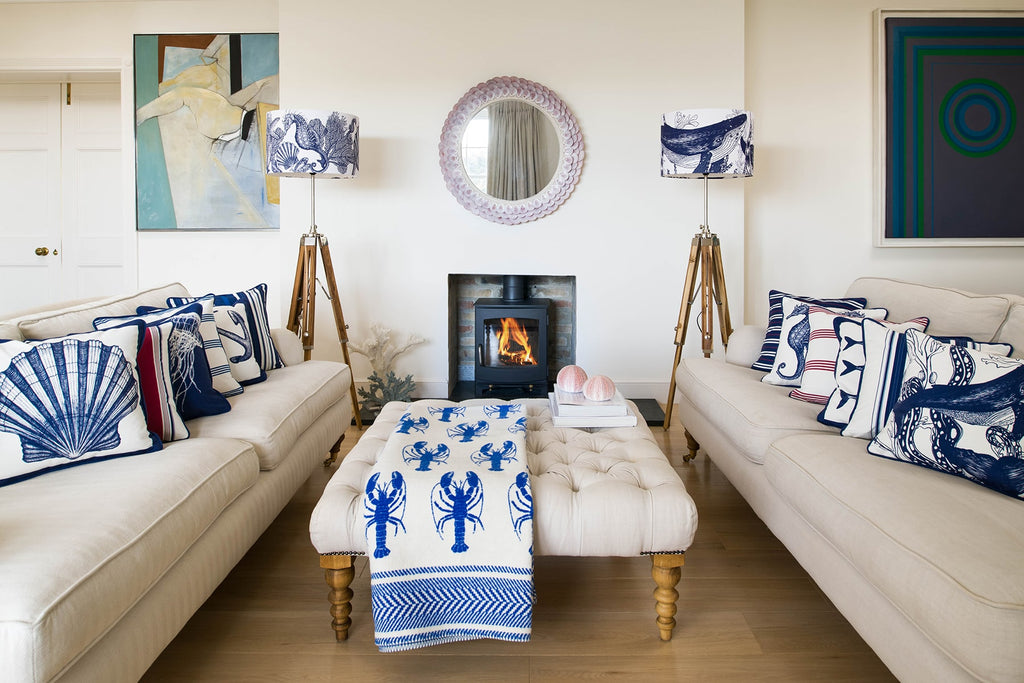 Our Classic Navy Seahorse design on a white background on a tripod stand on one side of a fireplace,there is another tripod with a navy Whale lampshade on the other side.In the photo are two large white sofas with our classic cushions placed on them.There is a wood burner in the fireplace and there is a footstool in the middle of the sofas.
