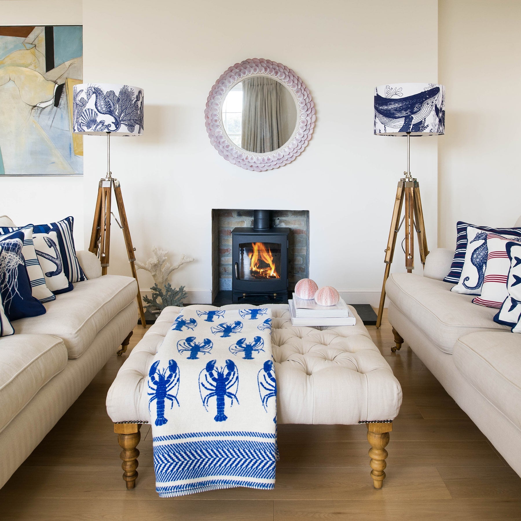 Our Classic Navy Whale design on a white background on a tripod stand on one side of a fireplace,there is another tripod with a navy Seahorse lampshade on the other side.In the photo are two large white sofas with our classic cushions placed on them.There is a wood burner in the fireplace and there is a footstool in the middle of the sofas.